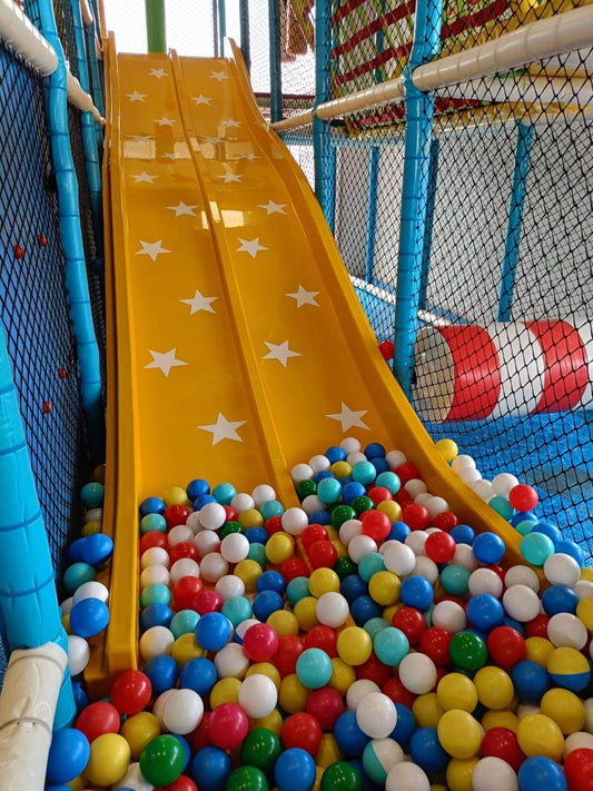 Bright yellow twin slides decorated with white stars ending in a colorful ball pit inside a secure play area