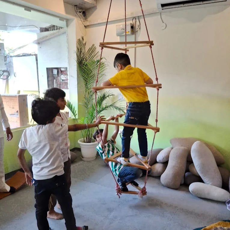 Children playing with a wooden swing in an indoor setting.