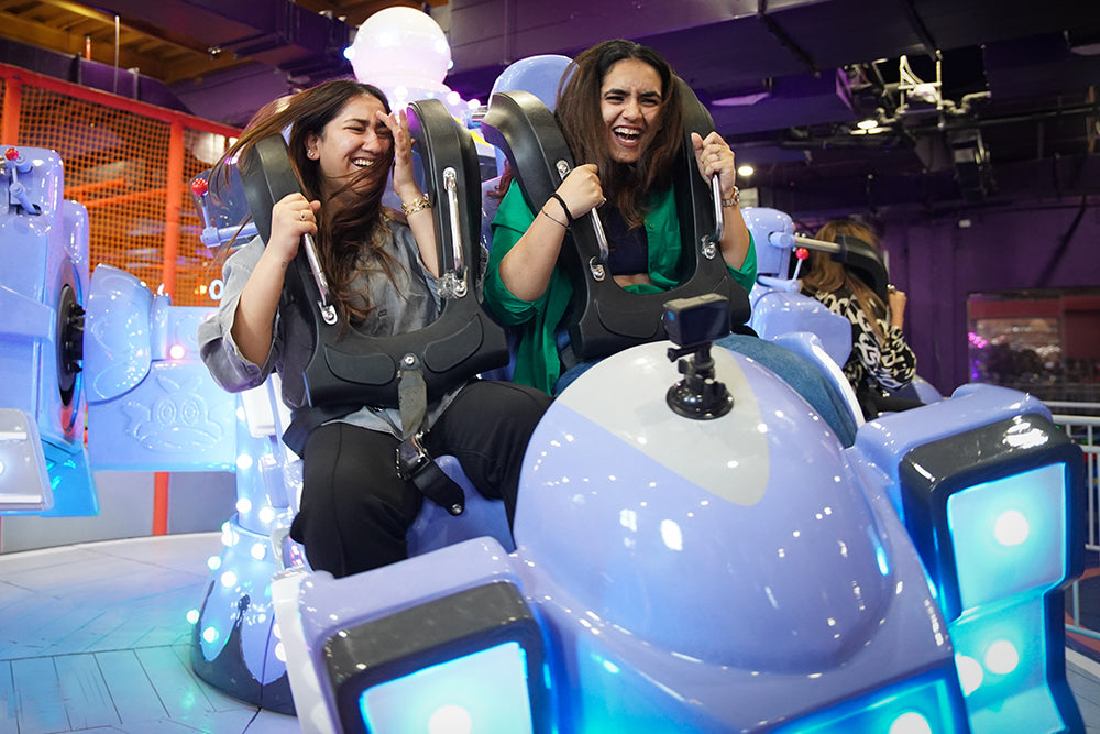 Two women enjoying a thrilling indoor amusement ride with vibrant blue lights at Boombastic Sector 62 Gurgaon event