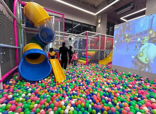 Children playing in a colorful ball pit with yellow and blue slides inside a safe indoor play area