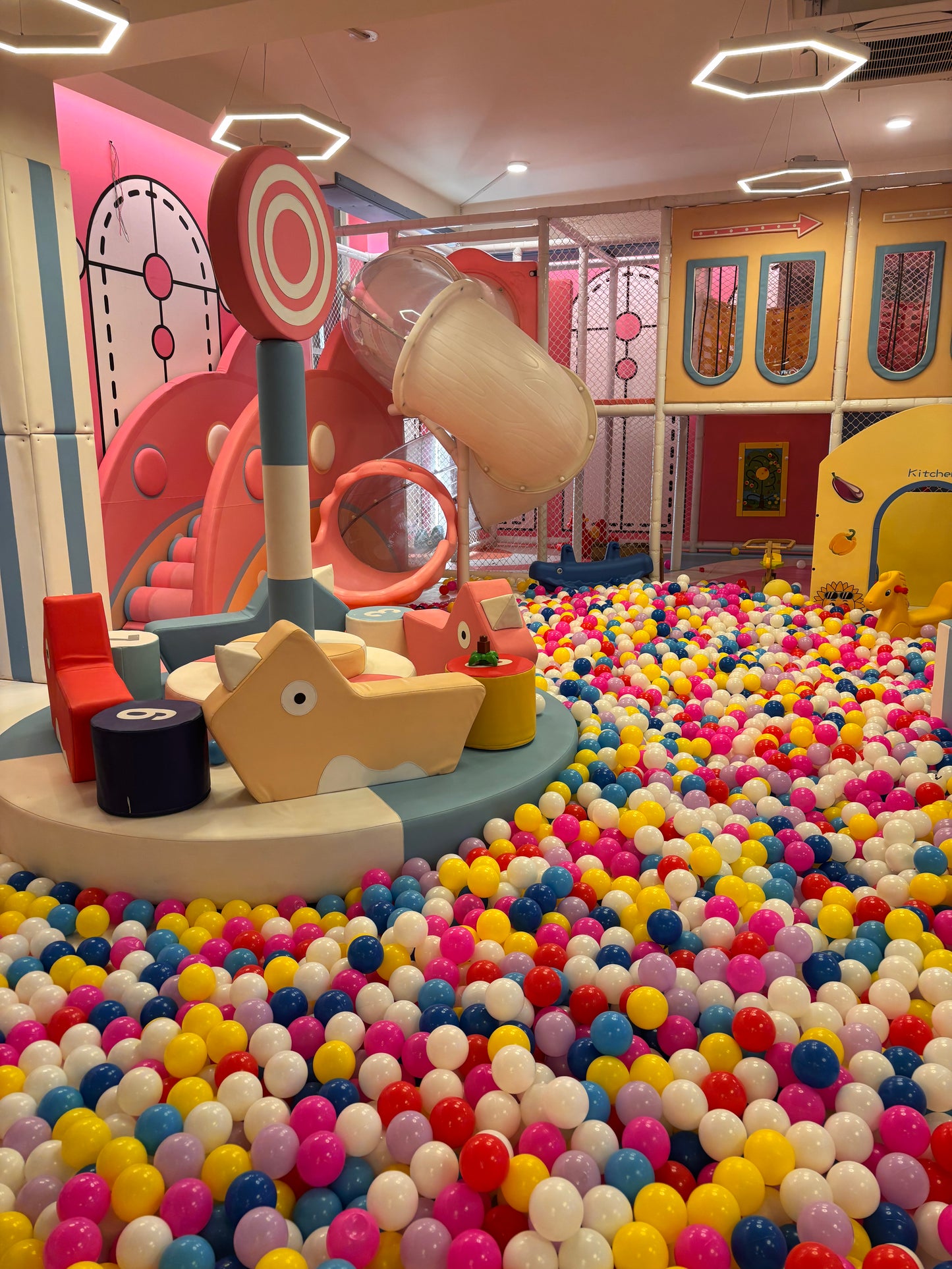 A colorful ball pit in a children's play area with slides and soft play structures.