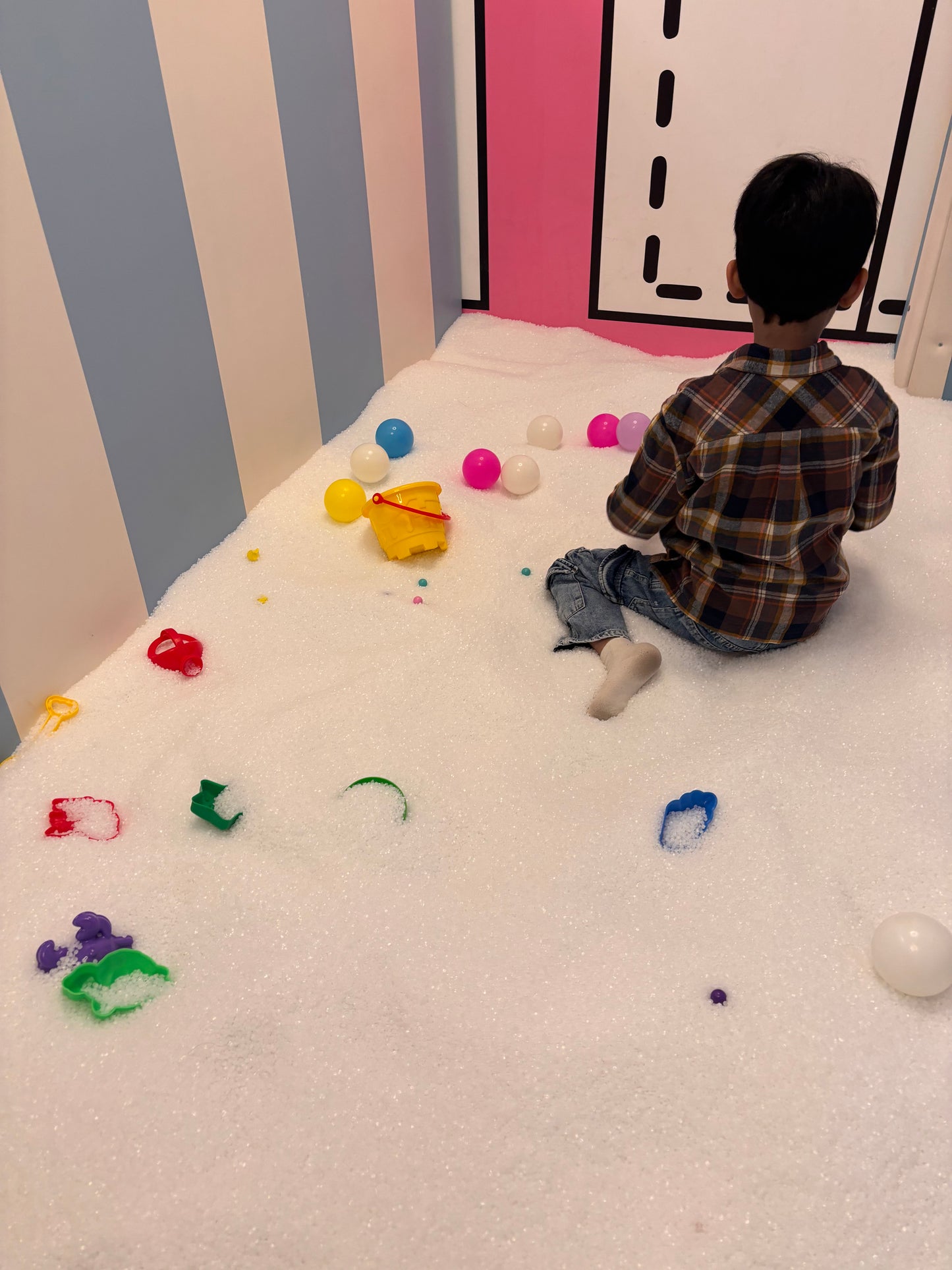 A young boy sits in a ball pit filled with white balls, playing with colorful toys.