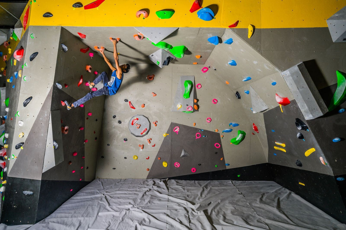 A young man bouldering on a colorful indoor climbing wall.