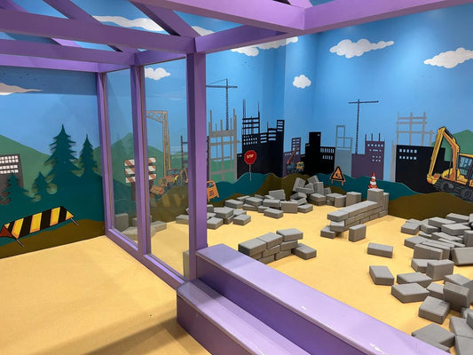 Children's play area with construction theme, featuring foam blocks and a mural.