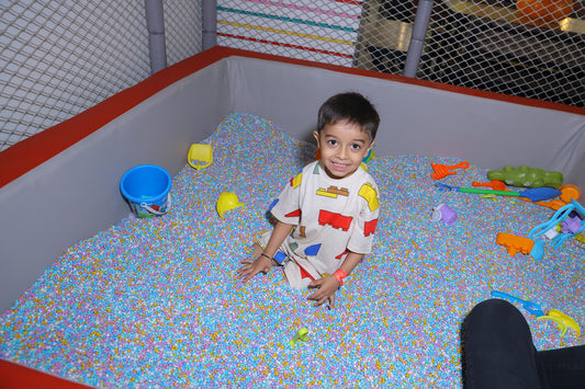 A young boy smiles while sitting in a ball pit filled with colorful balls and toys.