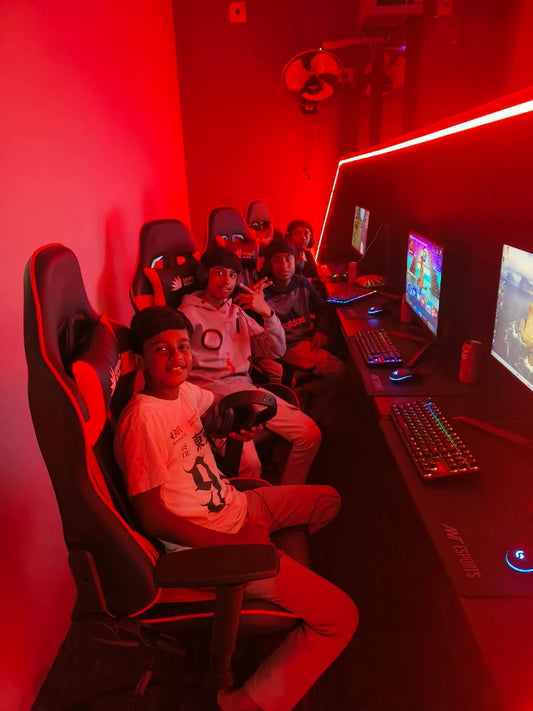 Young people play video games in a dimly lit room with red lighting and gaming chairs.