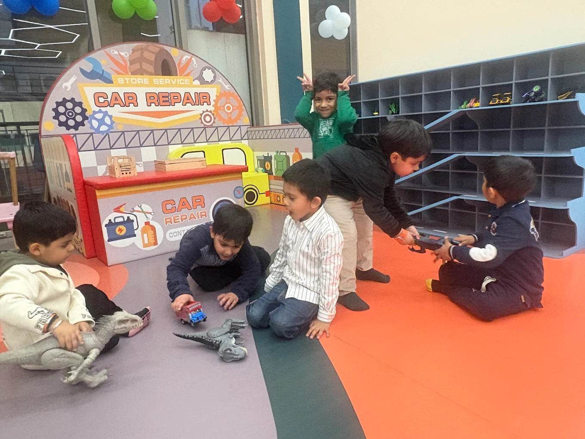 Young children play with toy cars and dinosaurs in a car repair themed play area.