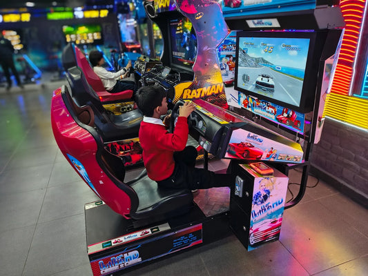 Two young boys play a racing arcade game in a dimly lit arcade.
