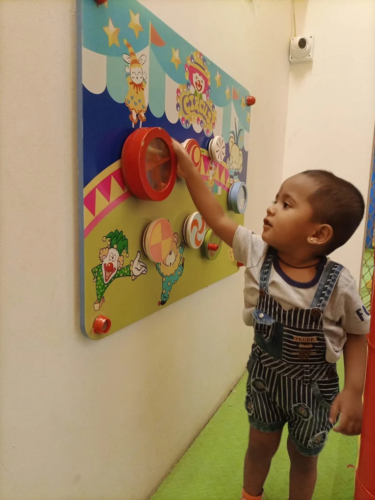A young child plays with a circus-themed interactive wall panel.