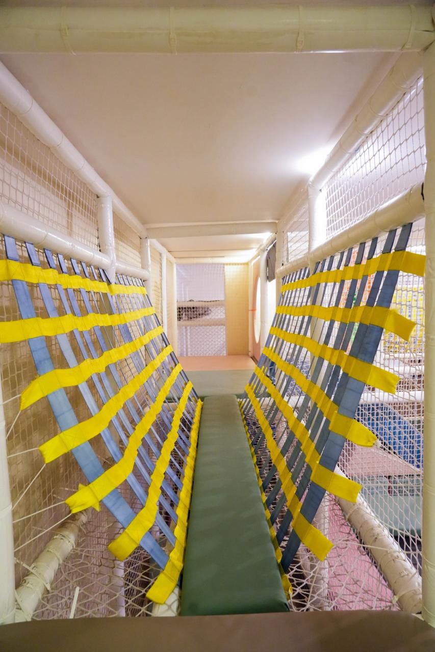 A padded walkway with yellow and blue netting in a children's indoor play area.