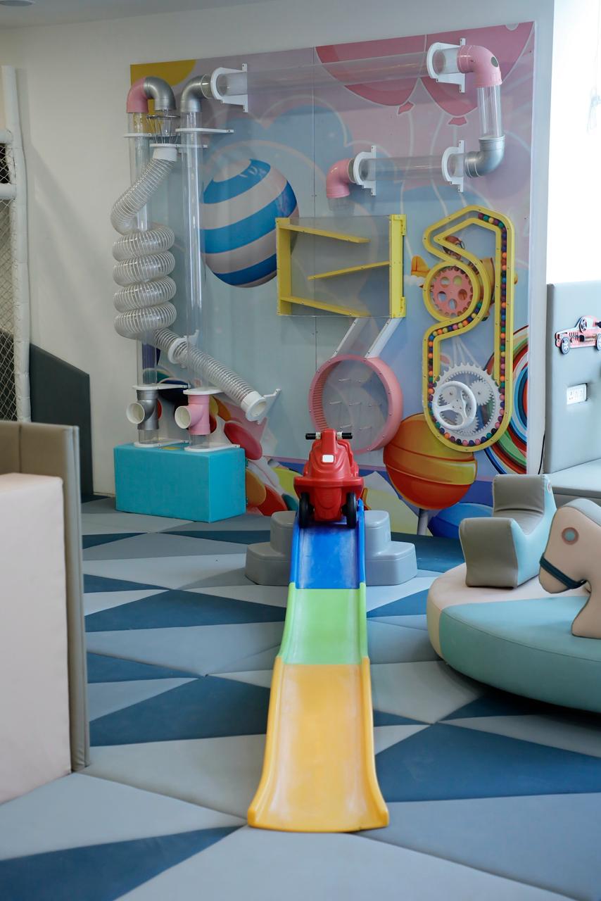 A colorful indoor playground with tubes, slides, and a toy car for young children.