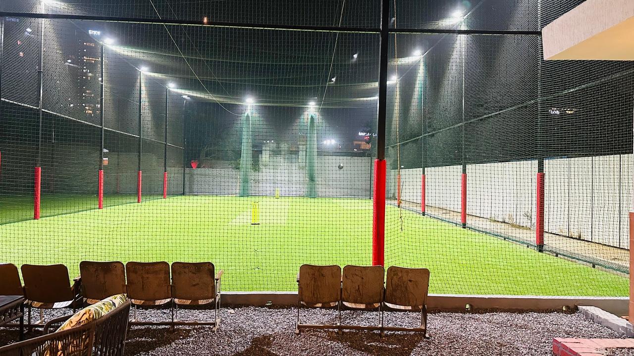 An illuminated outdoor cricket practice net with artificial turf and seating.