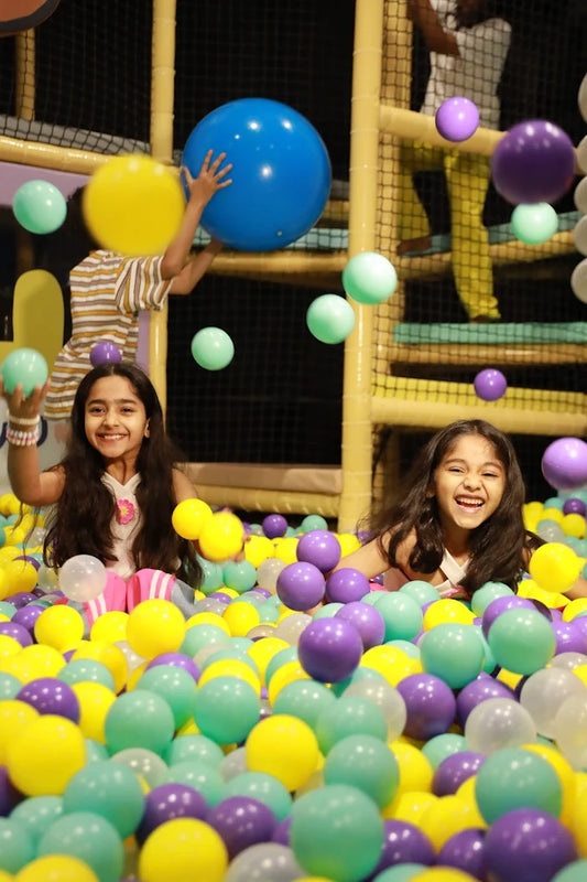 Two young girls laugh joyfully while playing in a ball pit filled with colorful balls.