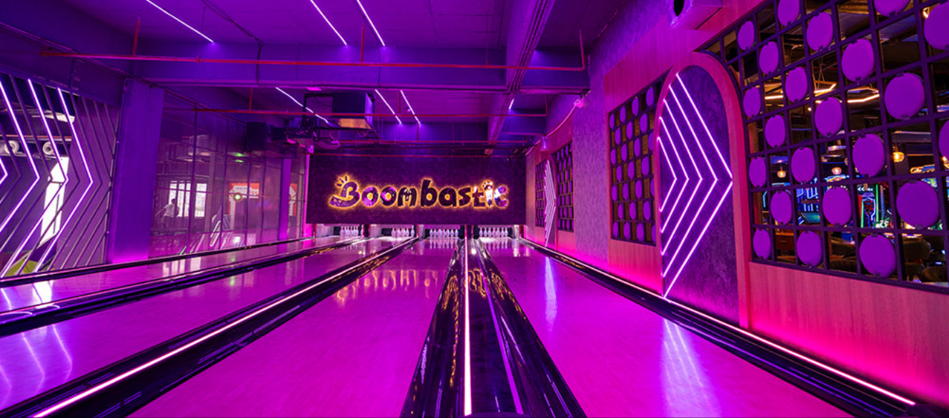 Vibrant purple-lit bowling lanes with neon decorations and Boombastic sign at Sector 62 Gurgaon Christmas Carnival venue