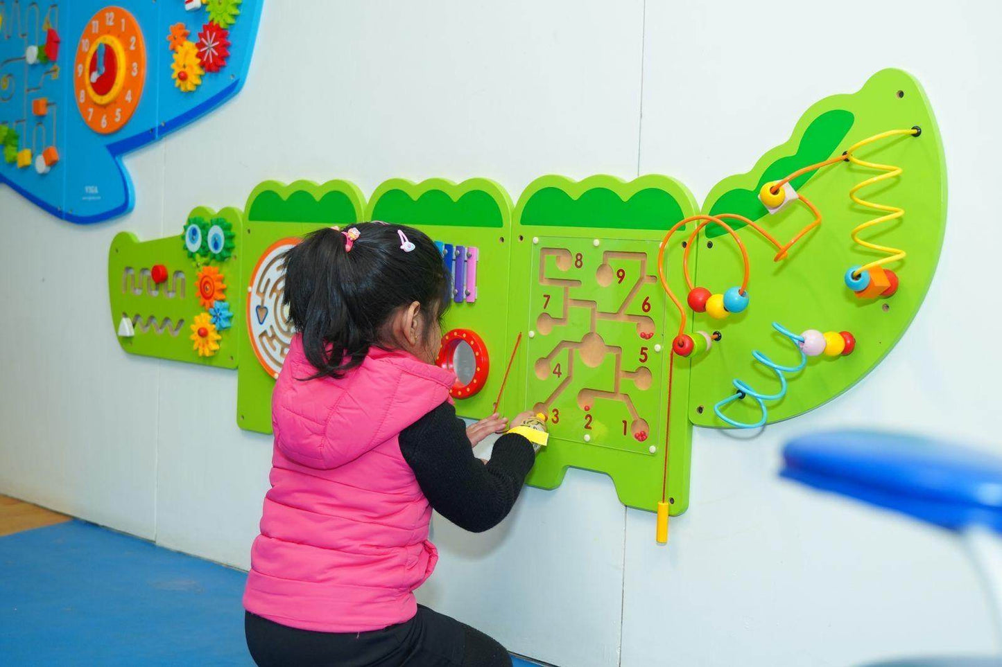 A young girl plays with a colorful, interactive wall toy featuring numbers and bead mazes.