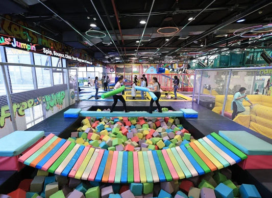 Children play in a colorful indoor trampoline park with foam pits and obstacle courses.