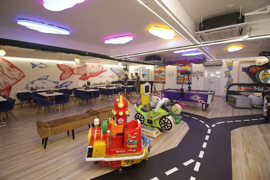 Indoor arcade playroom with ride-on toys and fish-themed wall art alongside seating at Anand Vihar Delhi