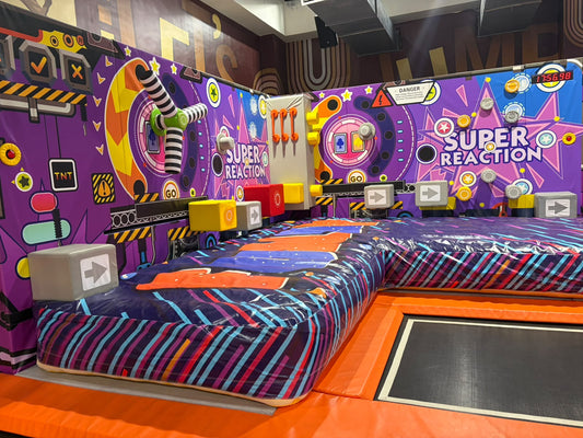 A colorful indoor trampoline park with a "Super Reaction" game. Children are playing on the bouncy surfaces.
