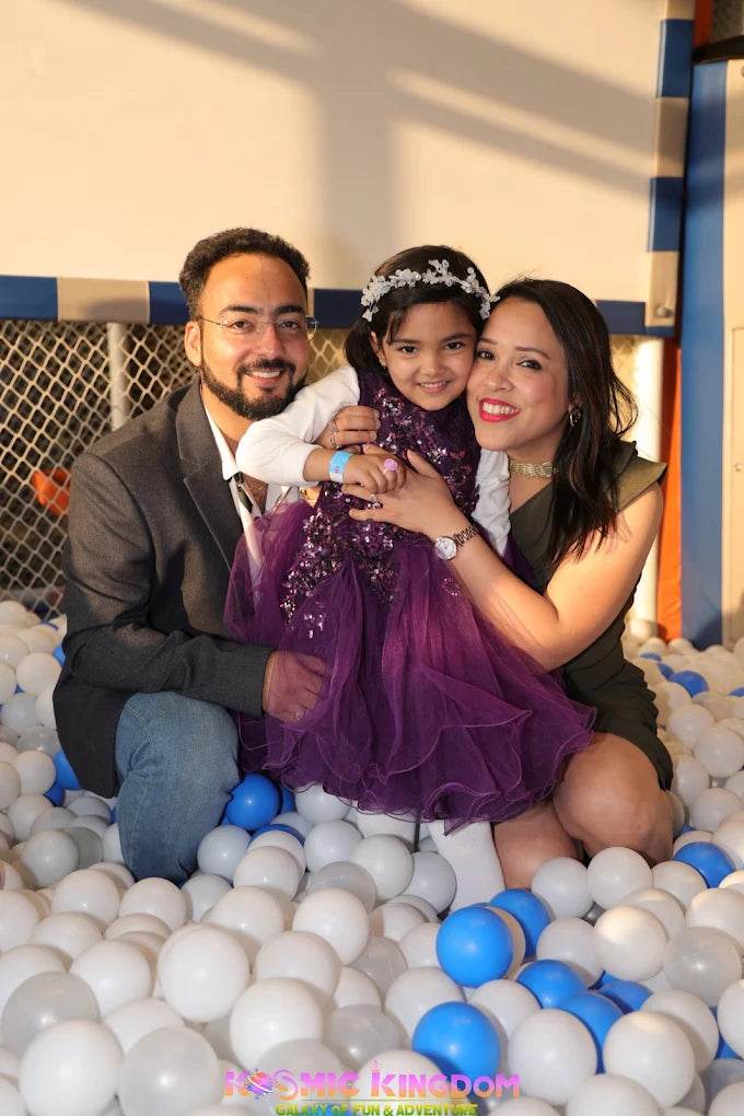A family poses in a ball pit, with a father, mother, and young daughter.
