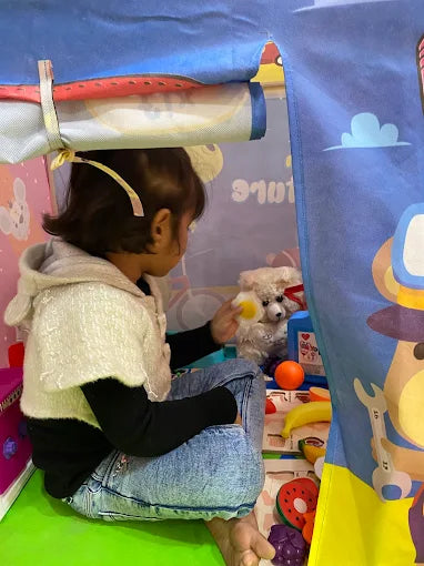 A young child plays with a stuffed dog inside a colorful play tent.