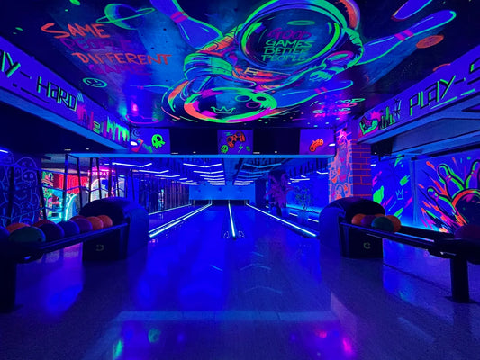 A neon-lit bowling alley with vibrant blacklight art and bowling balls ready for play.