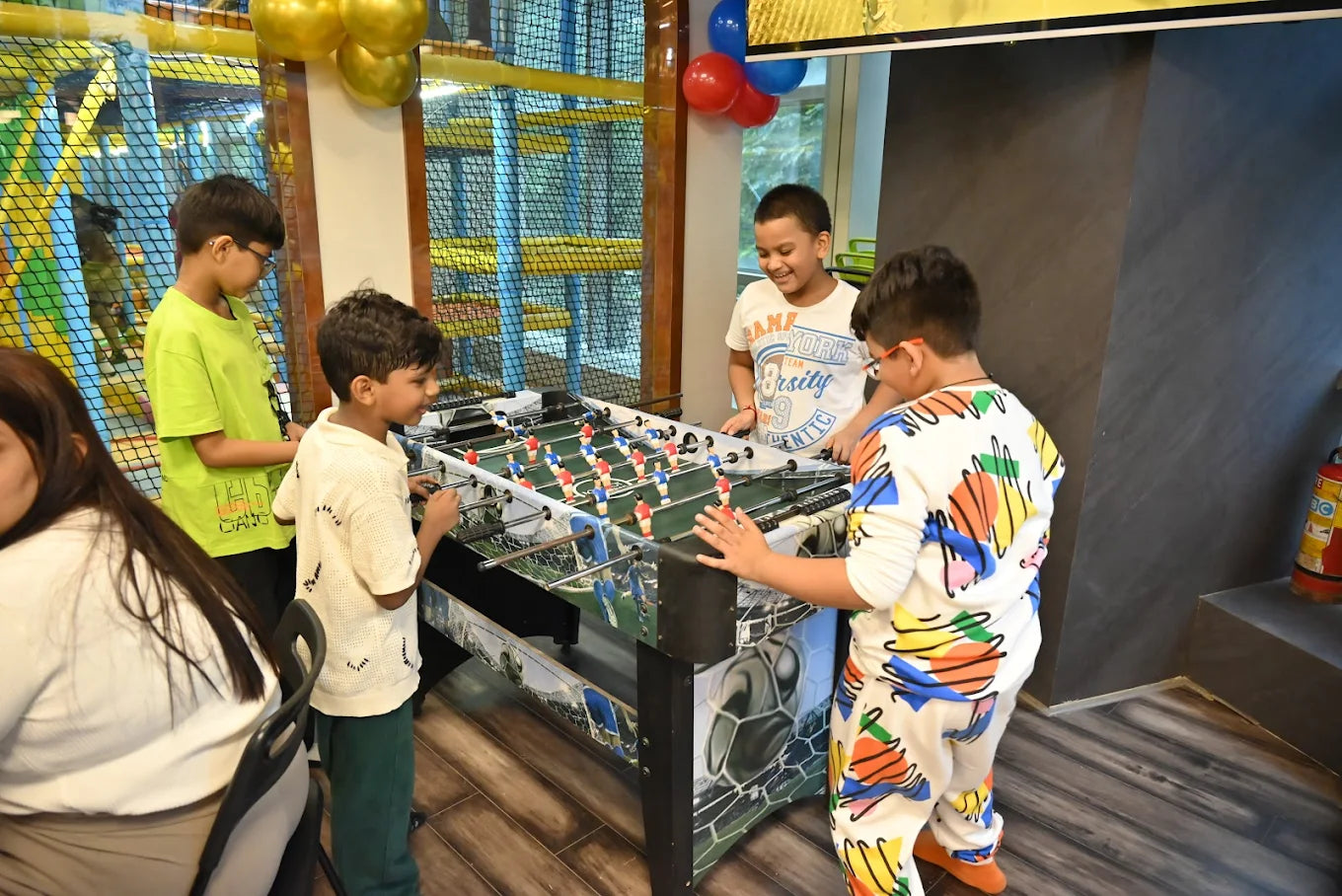 Children play foosball in a brightly decorated indoor play area.