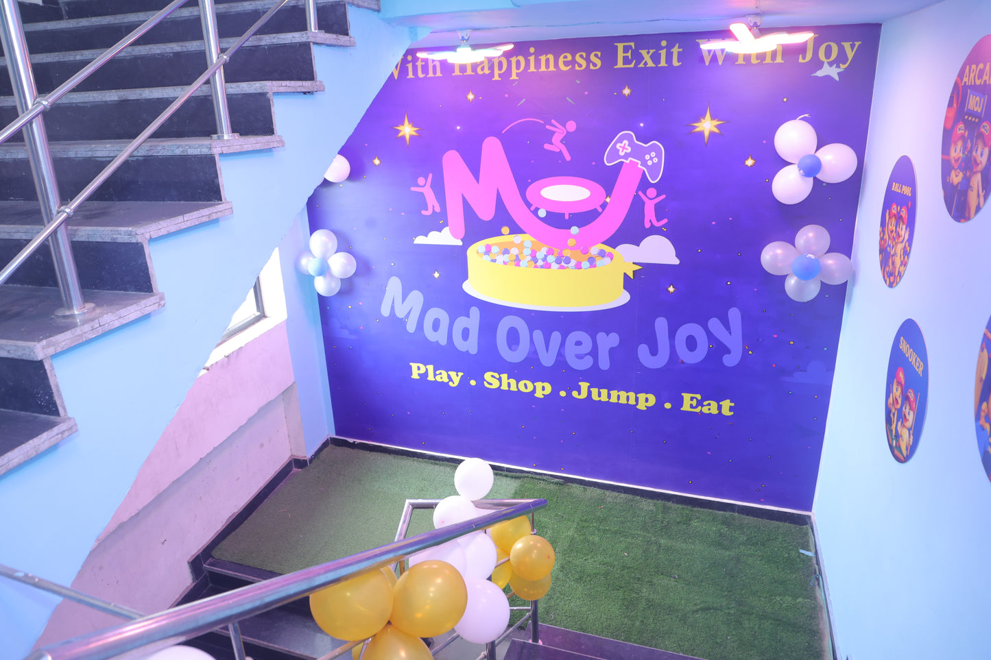 A colorful indoor play area with a ball pit, arcade games, and balloons, featuring a staircase.