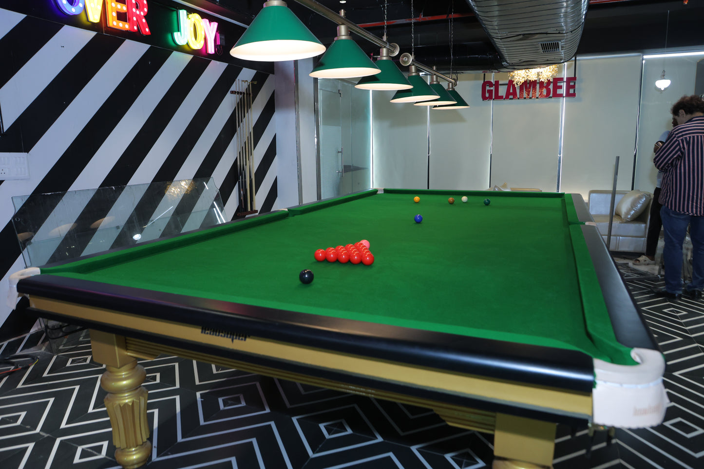 A snooker table with balls is set up in a room with neon signs and a person standing nearby.