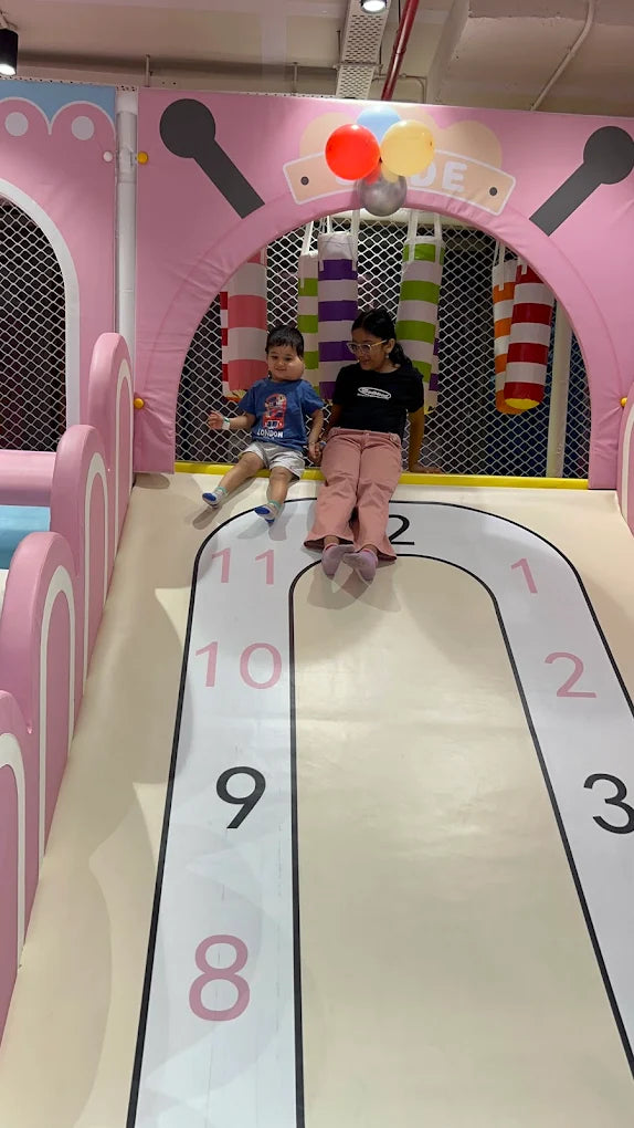 Two children sit on a slide in a colorful indoor playground.