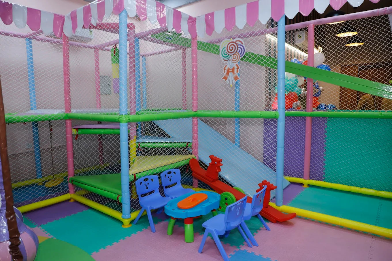 A colorful indoor playground with slides, a ball pit, and small chairs and tables for young children.