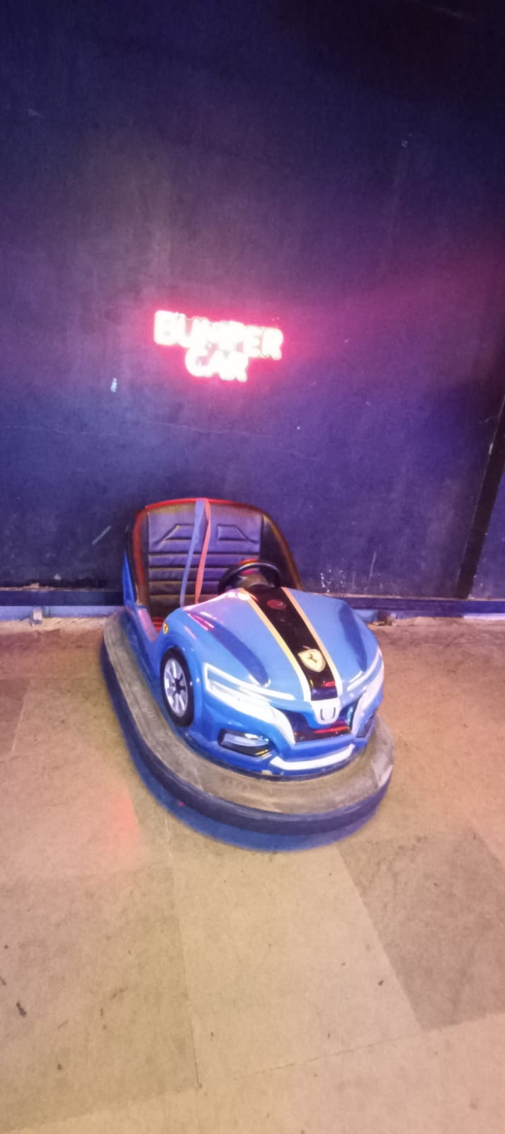 A blue bumper car sits in front of a neon "BUMPER CAR" sign.
