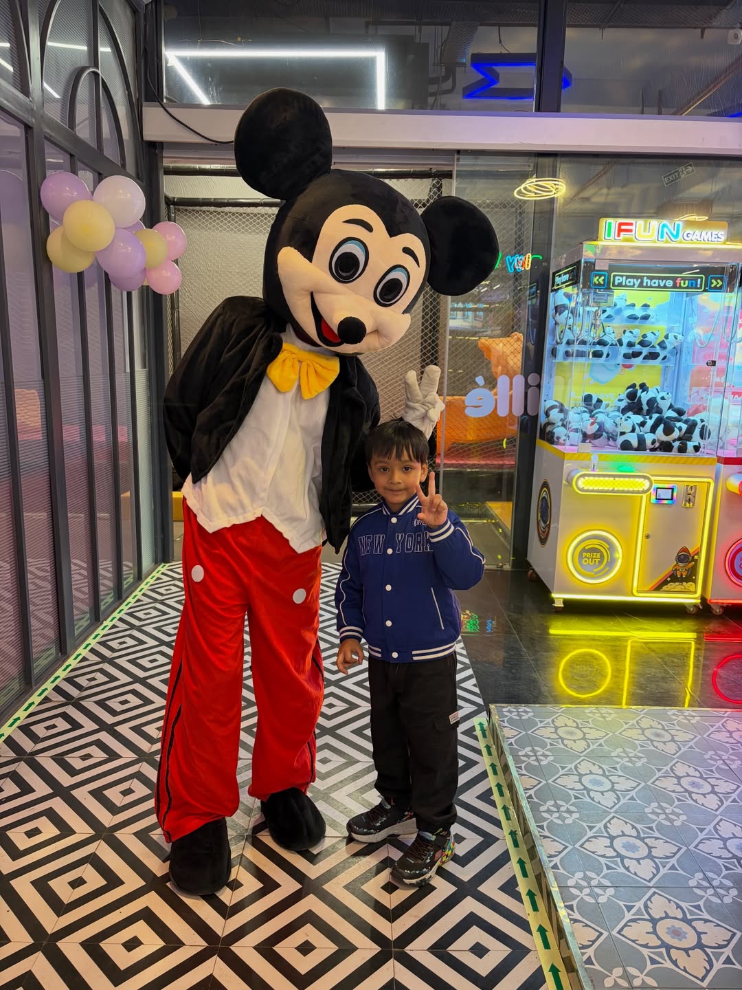 A child poses with a Mickey Mouse mascot in an arcade.