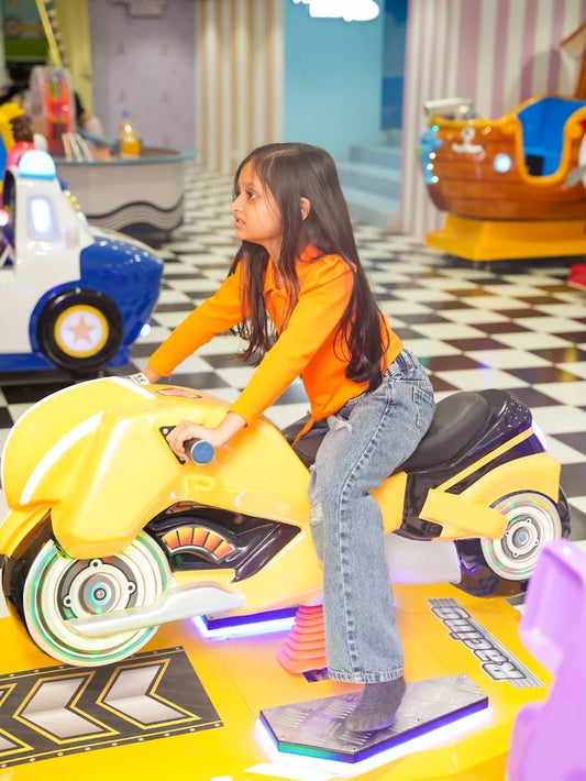 A young girl rides a yellow motorcycle arcade game in an amusement center.
