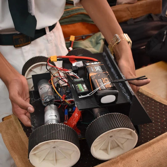 Student holding a small robot or electronic device with wheels on a wooden surface.