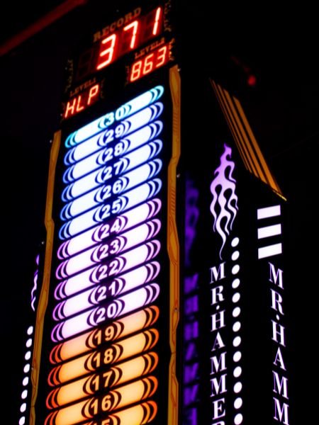 A tall, brightly lit tower displays a game's record score and levels, with numbers from 15 to 30 visible.