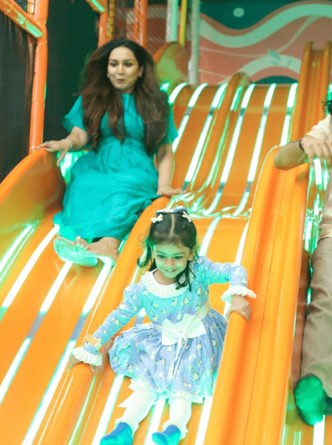 A woman and a young girl slide down an orange playground slide.
