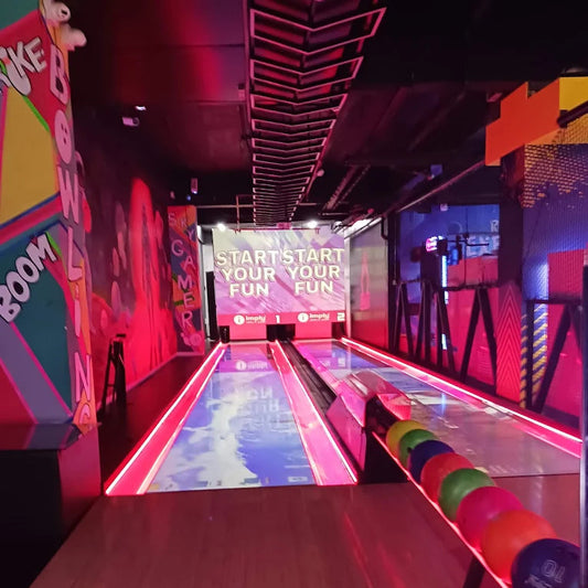 Indoor bowling alley with colorful walls and a screen displaying 'Start Your Fun Fun Fun'.