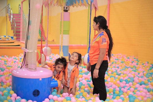 Woman and two children in a colorful ball pit with playground equipment in the background