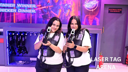 Two young women in laser tag vests hold phasers in an arena, ready to play.