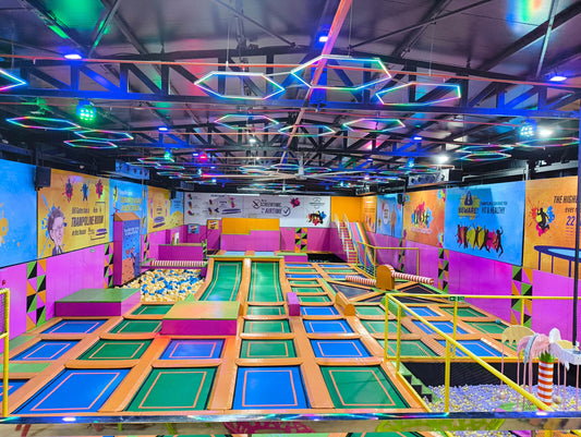 Vibrant indoor trampoline park with colorful jumping zones, foam pits, and geometric neon ceiling lights at Dwarka Expressway Gurgaon location