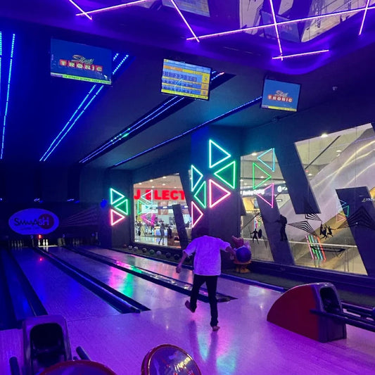 A person bowls in a neon-lit entertainment center with bowling lanes and screens.