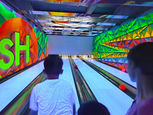 Two players bowling on lanes illuminated by vibrant geometric neon patterns at Smaaash Sector 13 Dwarka Delhi