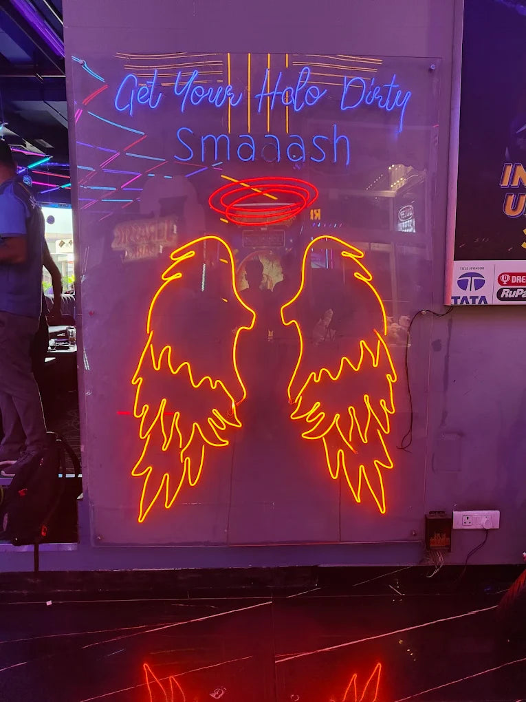 Neon angel wings and text "Get Your Halo Dirty Smaaash" in a dimly lit venue.