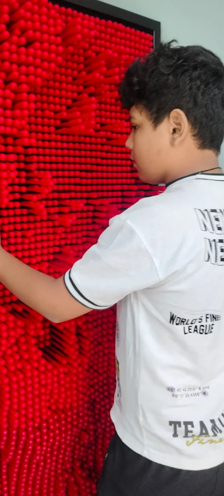 A young person interacts with a red pin art toy, creating a 3D impression.