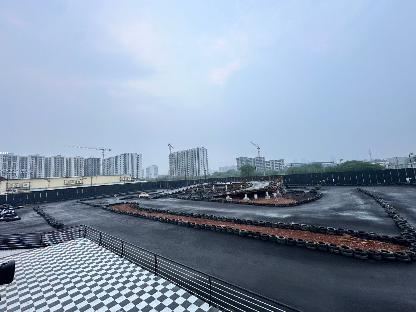 A go-kart track with a checkered floor area and buildings in the background.