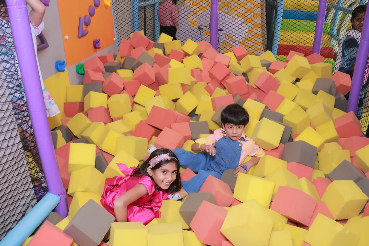 Two children play in a ball pit filled with colorful foam cubes.