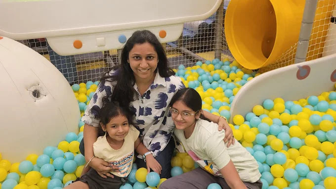 Smiling woman with two children sitting in a colorful ball pit next to white and yellow slides at Punjabi Bagh Club