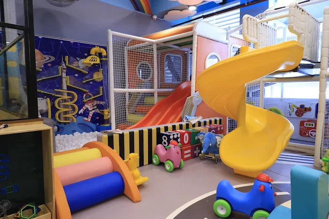 Indoor children’s play area with spiral yellow slide, soft play structures, and colorful ride-on toys at Punjabi Bagh Club