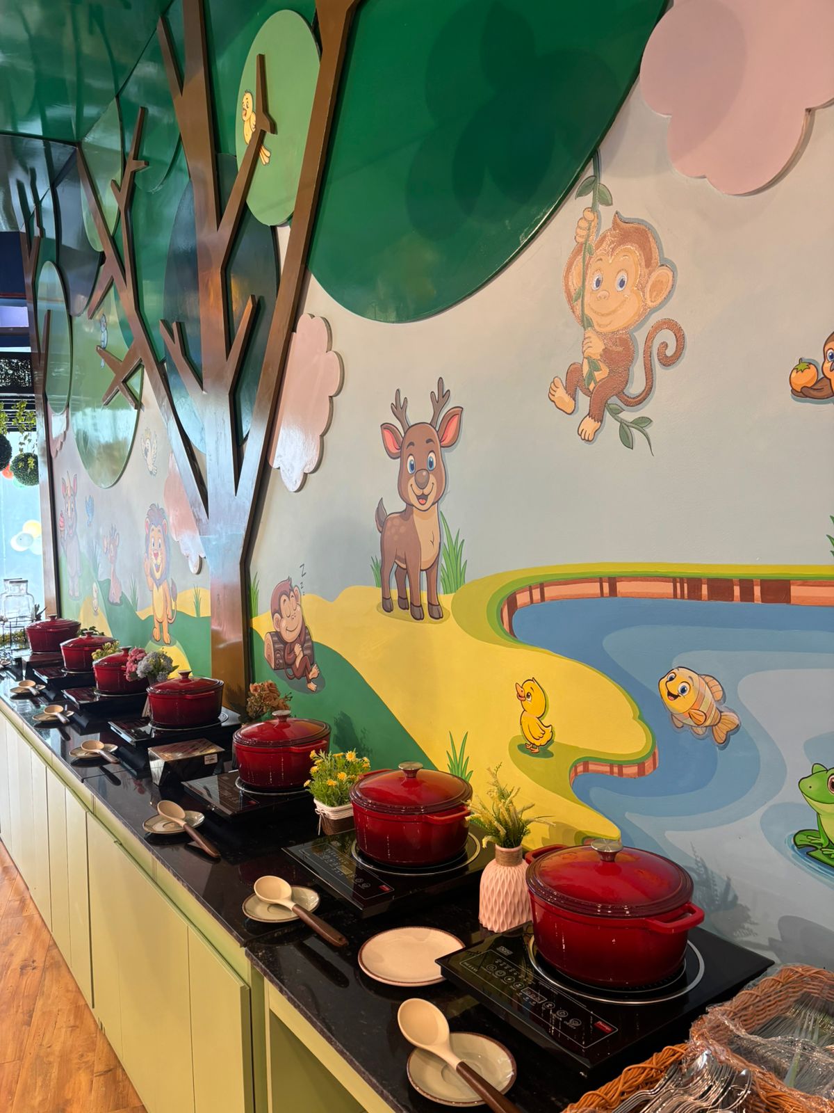 Indoor buffet setup with red pots and playful animal wall art including monkey and deer at Tooney Tales Noida event