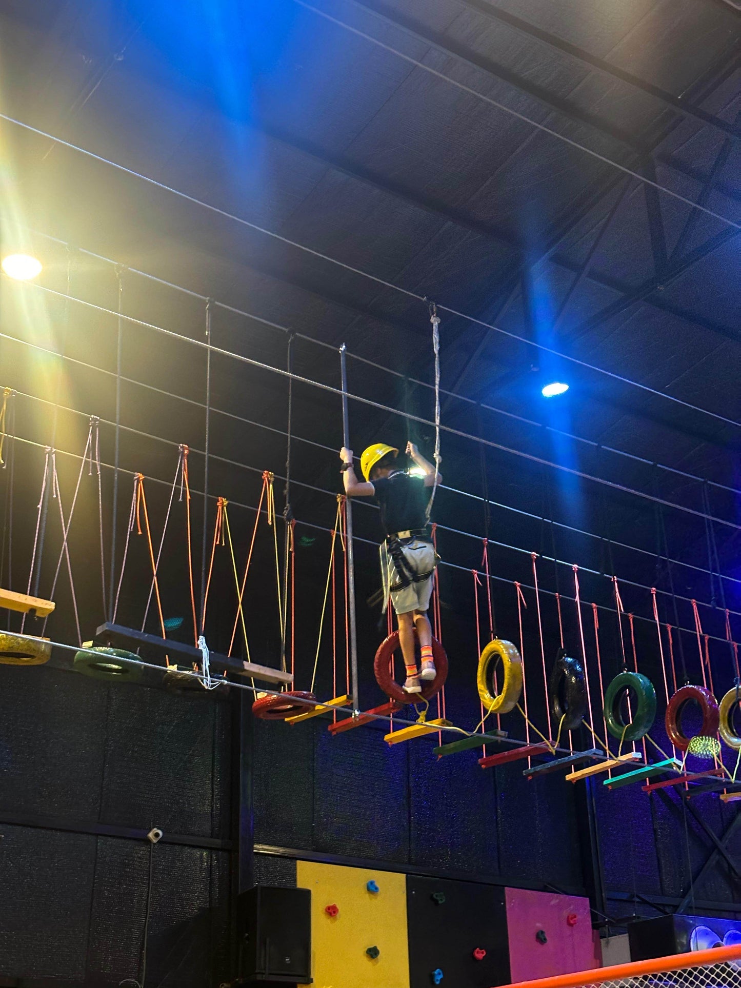 Child wearing helmet navigating suspended obstacle course with colorful tires at indoor adventure carnival in Trumpy Sector 83 Gurgaon